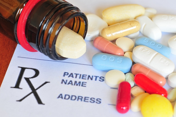 Brown medicine bottle on its side with pill spilling out, surrounded by colorful pills and Rx prescription pad