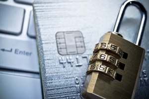 A credit card with a chip rests on a keyboard beside a combination padlock, symbolizing online security and data protection.