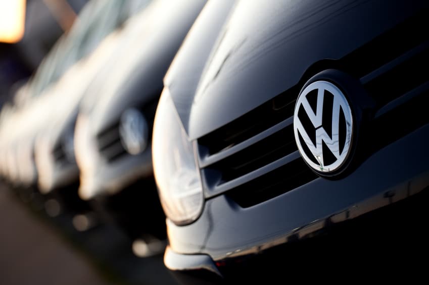 Close-up of a Volkswagen car front with VW emblem and parked vehicles in background.