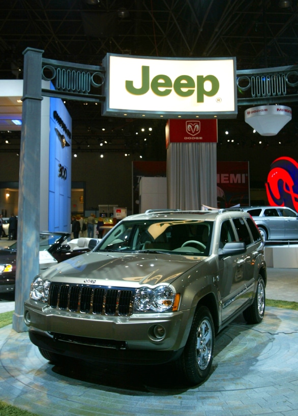 A Jeep SUV is displayed under a large Jeep sign at an indoor auto show, surrounded by other vehicles and brand displays.