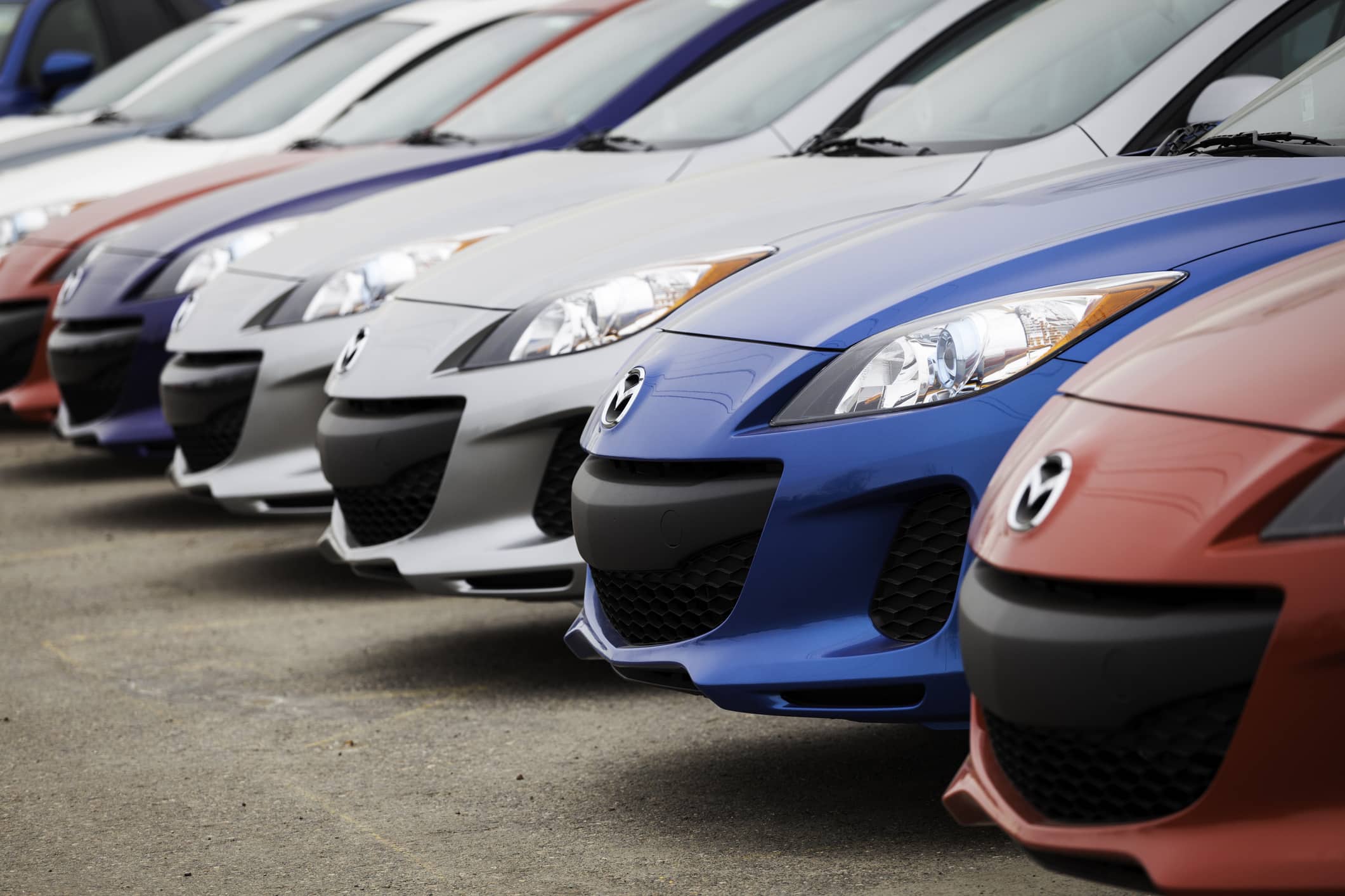 Front-angle view of a line of multi-colored cars, including red, blue, and silver, parked closely together.