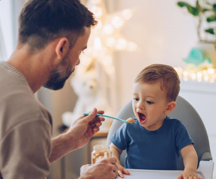 A man gently feeds his young son a spoonful of food, showcasing a moment of care and nurturing between them.