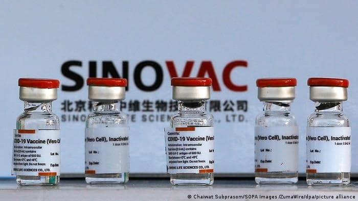 Vials of Sinovac COVID-19 vaccine lined up with Sinovac logo and company name in the background.