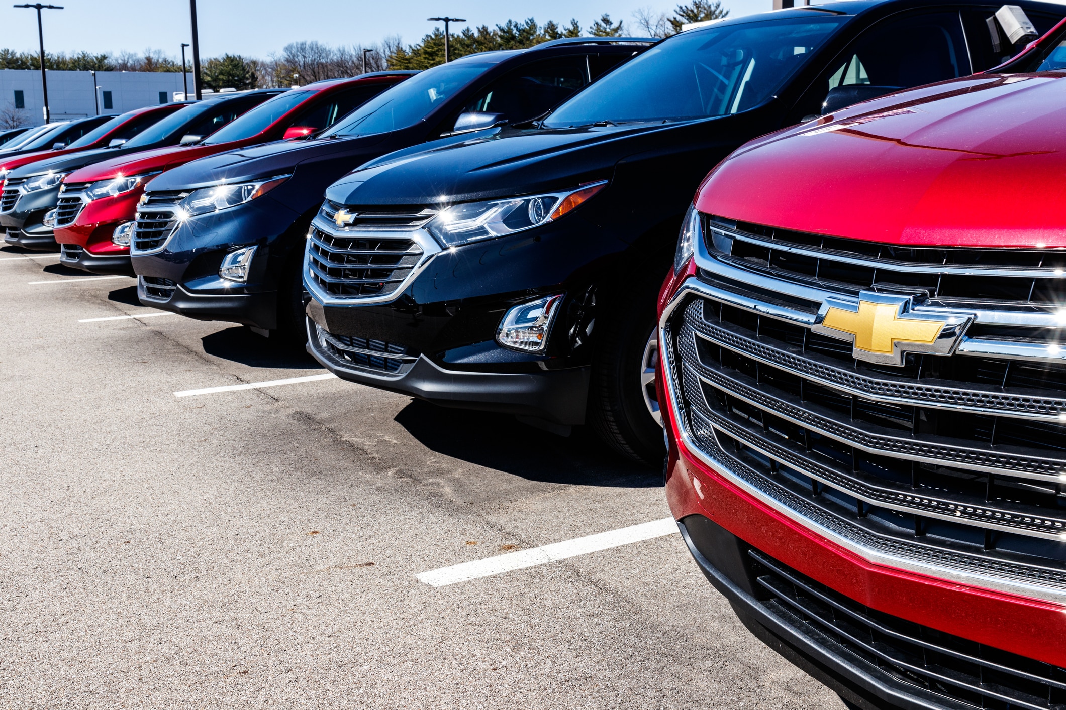 Front view of new Chevrolet SUVs in red, black, blue, and grey, parked in a row at an outdoor dealership lot.