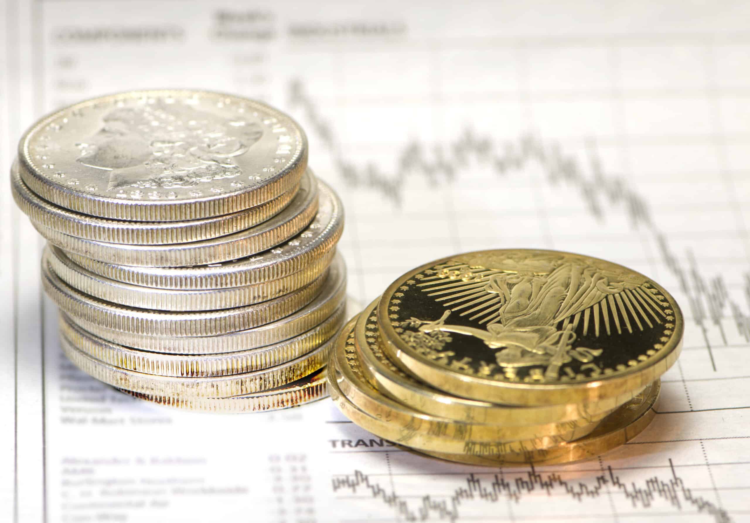 Conceptual image with stacks of silver and gold coins next to a graph showing a sharply declining stock market.