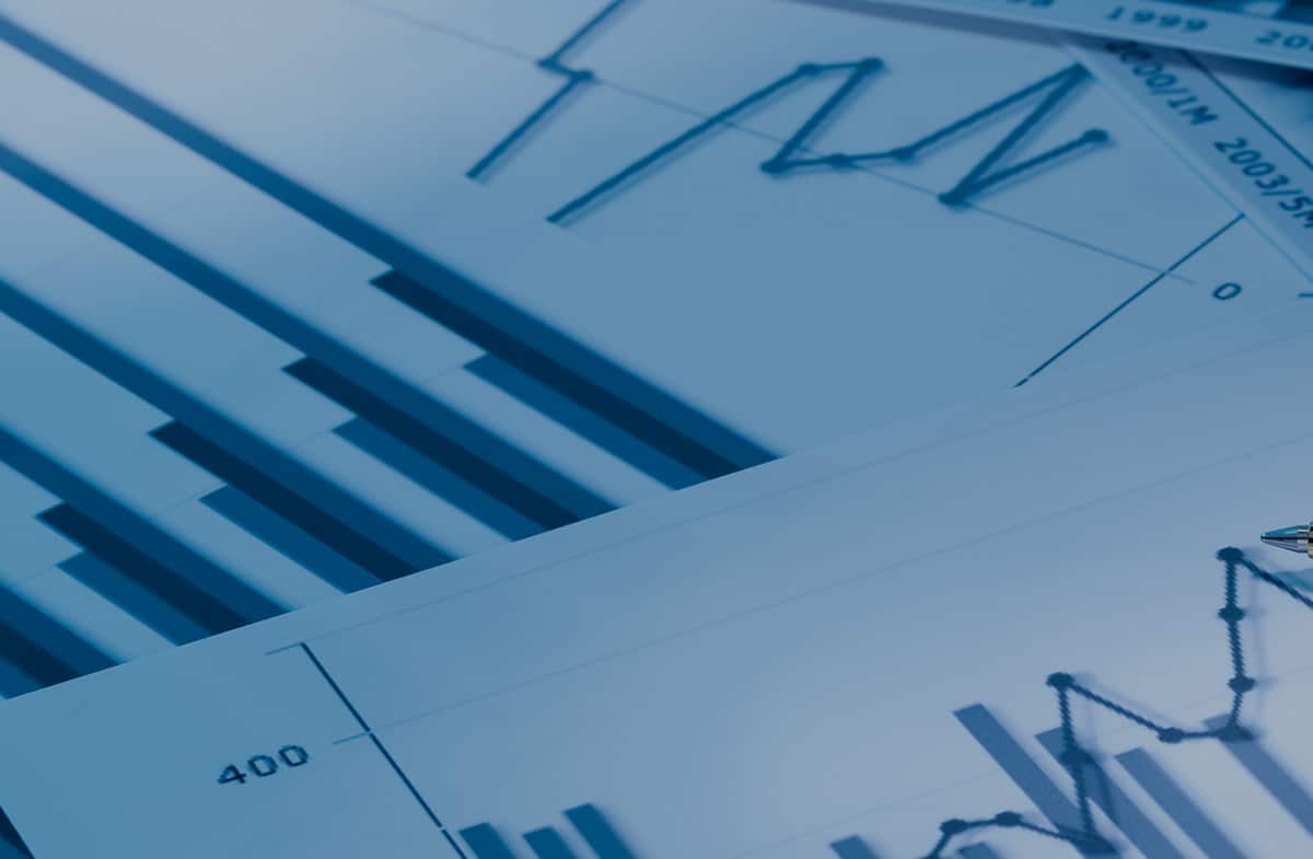 Close-up of financial bar and line graphs on overlapping papers with pen tip