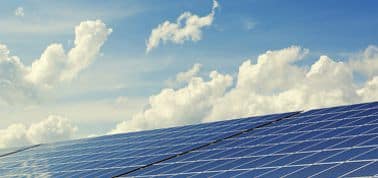 Solar panels angled under a blue sky with fluffy clouds. The image conveys a sense of clean energy and sustainability, highlighting renewable power.