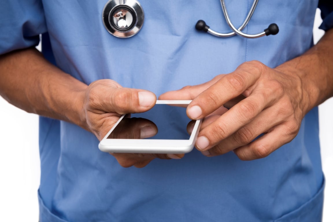 Medical professional in blue scrubs with stethoscope holding a white smartphone