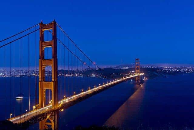 Golden Gate Bridge at night, illuminated, spanning bay with city lights under dark blue sky