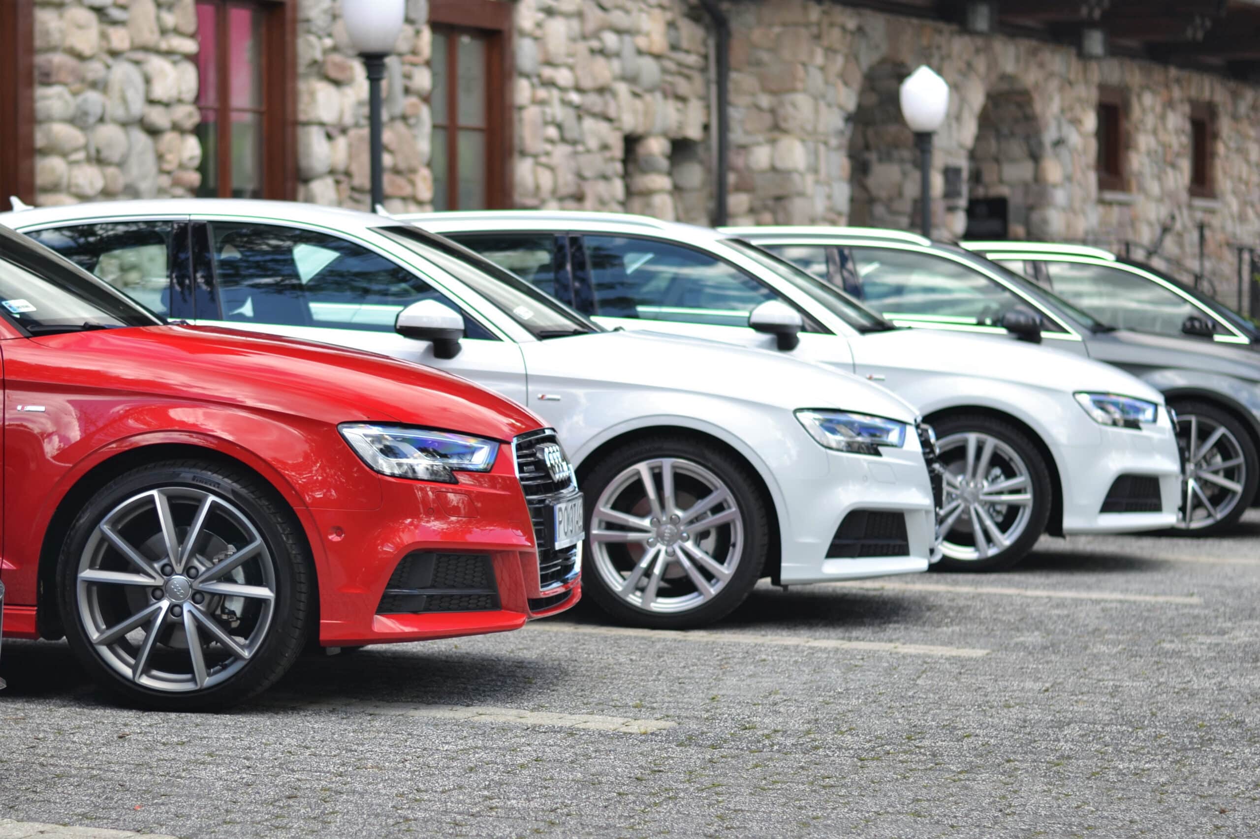 Five Audi cars parked in a row on pavement with stone building background