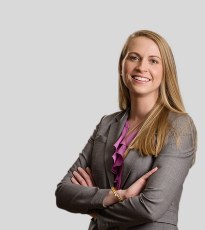 Professional headshot of a woman with long blonde hair wearing a gray blazer, arms crossed.