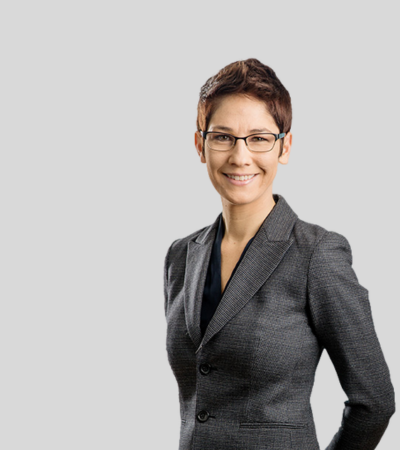 Stacey M. Kaplan Bioimage Woman with short hair and glasses, gray blazer, smiling.
