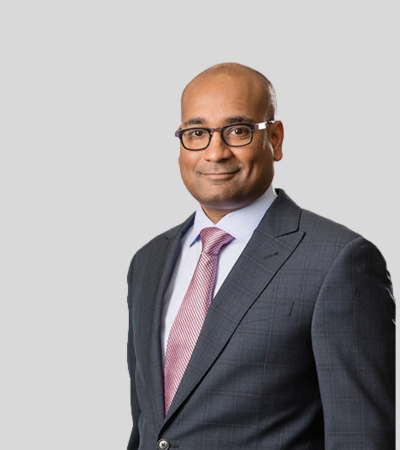 Sharan Nirmul Man in gray suit with pink tie, slight smile.