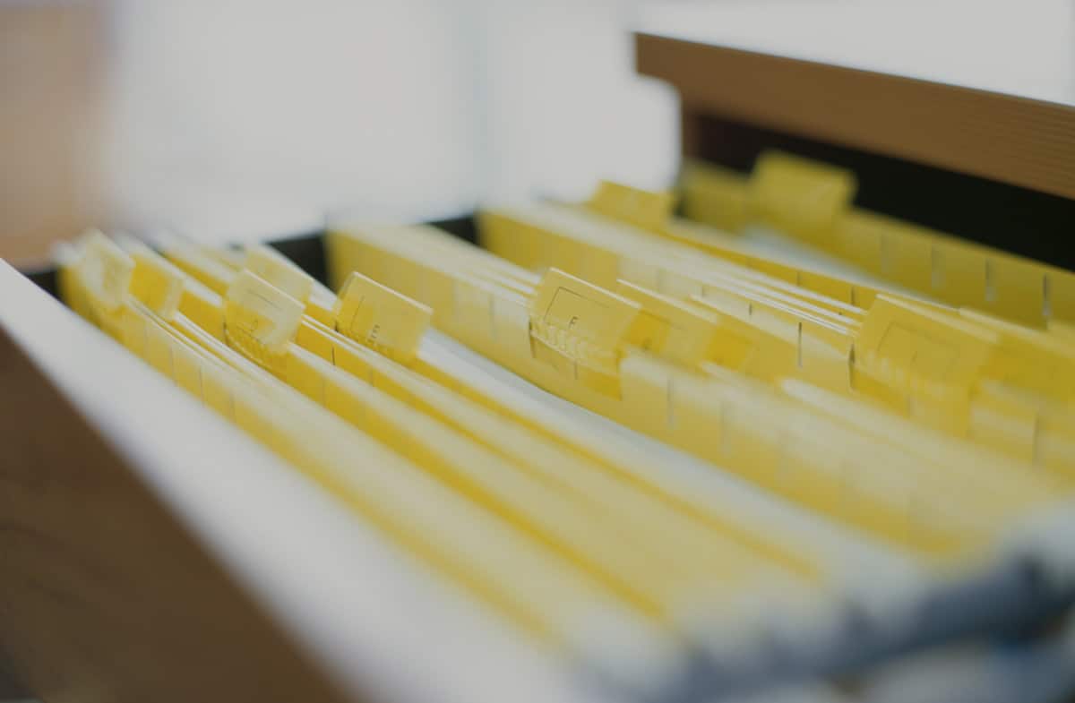 Close-up of yellow file folders with labeled tabs arranged inside a filing cabinet drawer, symbolizing document organization and records management.