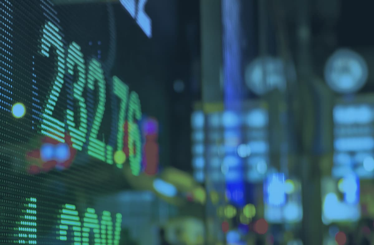 Blurred digital stock market ticker display with financial numbers and city lights in the background.