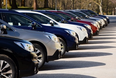 Front-left view of black, silver, blue, white, and red SUVs parked outdoors with long shadows