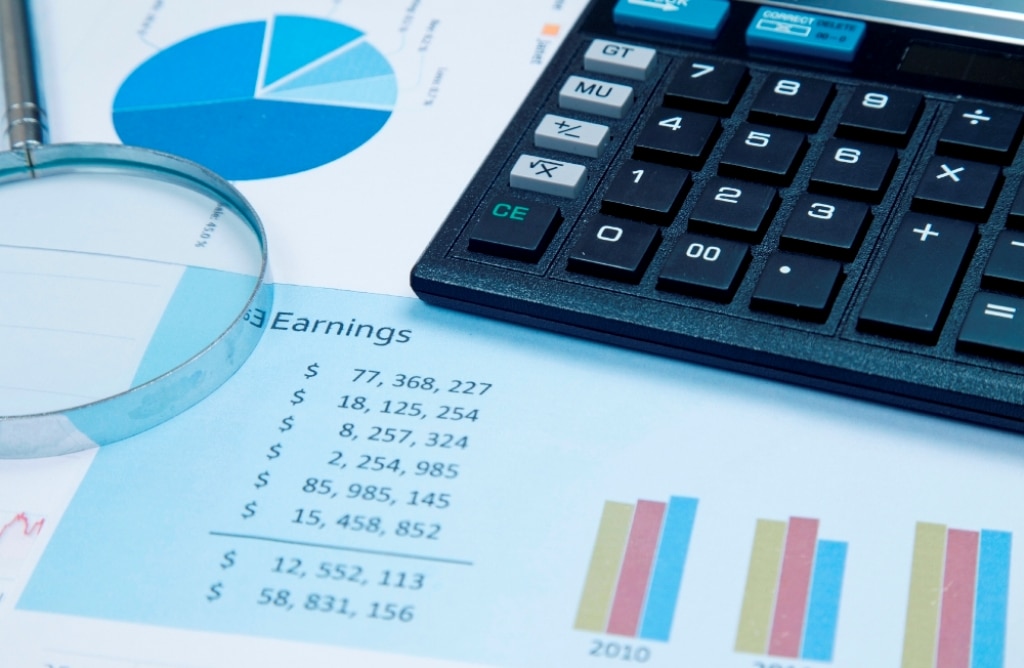 Calculator and magnifying glass resting on a financial document showing charts and 'Earnings' data.